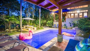 A pool area with lounge chairs, a flamingo float, and a hot tub. - Sonidos Del Mar - Tropical Garden Villa (Jaco)