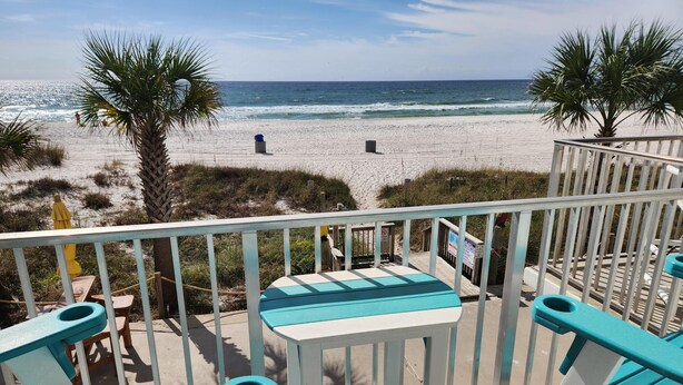 Blick auf einen Strand mit einer Terrasse, bequemen, türkisblauen Stühlen und einem Tisch.