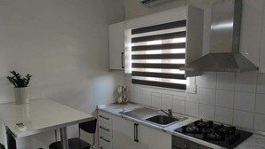 Una cocina con encimera blanca, un fregadero, una estufa y una ventana con persianas.