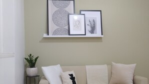 Una sala de estar en tonos neutros, con un sofá beige, una pequeña mesita con una planta en maceta y un estante de pared con obras de arte enmarcadas.