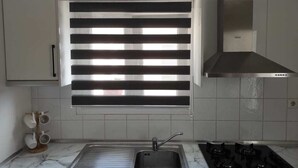 Una cocina con un lavamanos de acero inoxidable, una estufa a gas y una ventana con persianas horizontales.