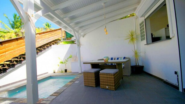 A covered outdoor area with a pool, wicker furniture, and a staircase leading to a wooden deck. - T2 Design for 2 with small private pool, ideal for a loving couple. (Les Trois ILets)