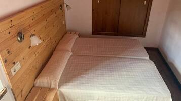 Huoneessa on puinen sängynpääty, valkoinen, kuviollinen peitto sängyllä, puinen vaatekaappi ja seinään kiinnitetty valaisin.