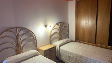 A bedroom with two single beds, a wooden wardrobe, and a bedside table with a lamp.
