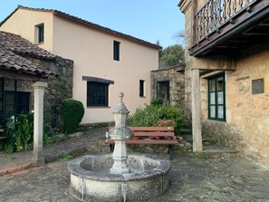 Un cortile con una fontana in pietra, una panchina e un edificio con tetto in tegole.
