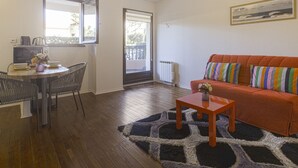Ein kompakter Wohnraum mit Essbereich, einer Couch und Blick durch eine Tür auf einen Balkon.