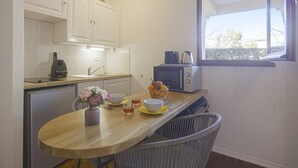 Eine kleine Küche mit weißen Schränken, einer Mikrowelle, einem Toaster und einem Fenster mit Blick auf Bäume.