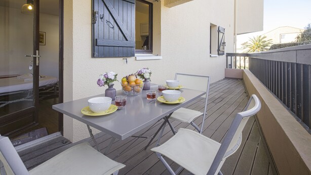 Ein Balkon mit Tisch für zwei Personen, Stühlen und einem kleinen Garten mit Blumen.