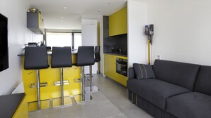 Et moderne køkken med gule skabe, en sort bordplade og en indbygget ovn. Der er en sort sofa med pude og et lille bord med stole.