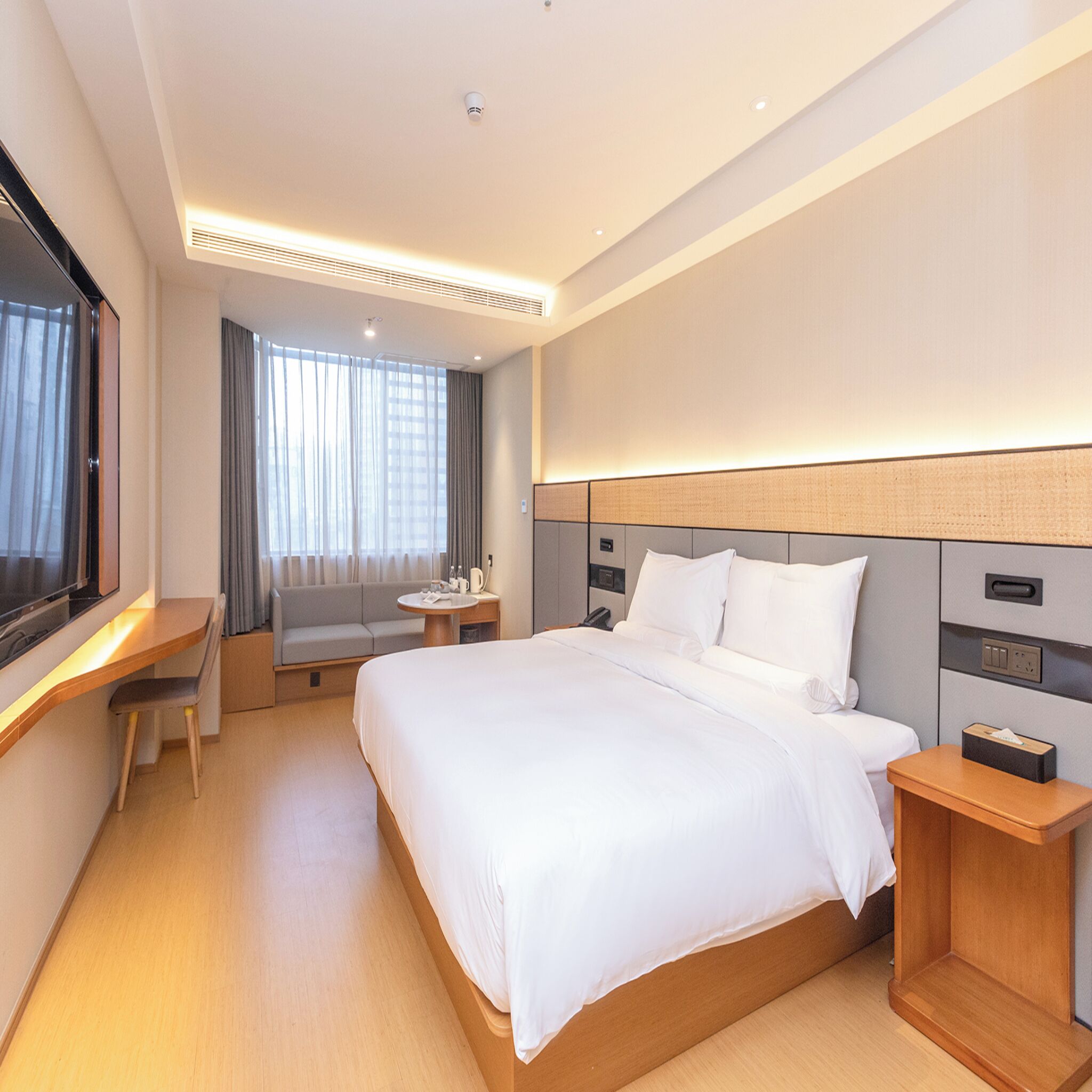 A hotel room with a bed, bedside tables, a desk, and a window with curtains.