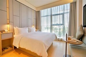 A hotel room with a large bed, bedside tables, a small sofa, and a view through large windows. - Ji Hotel (Shenzhen)
