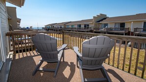 Un balcon avec des fauteuils Adirondack donnant sur une plage.