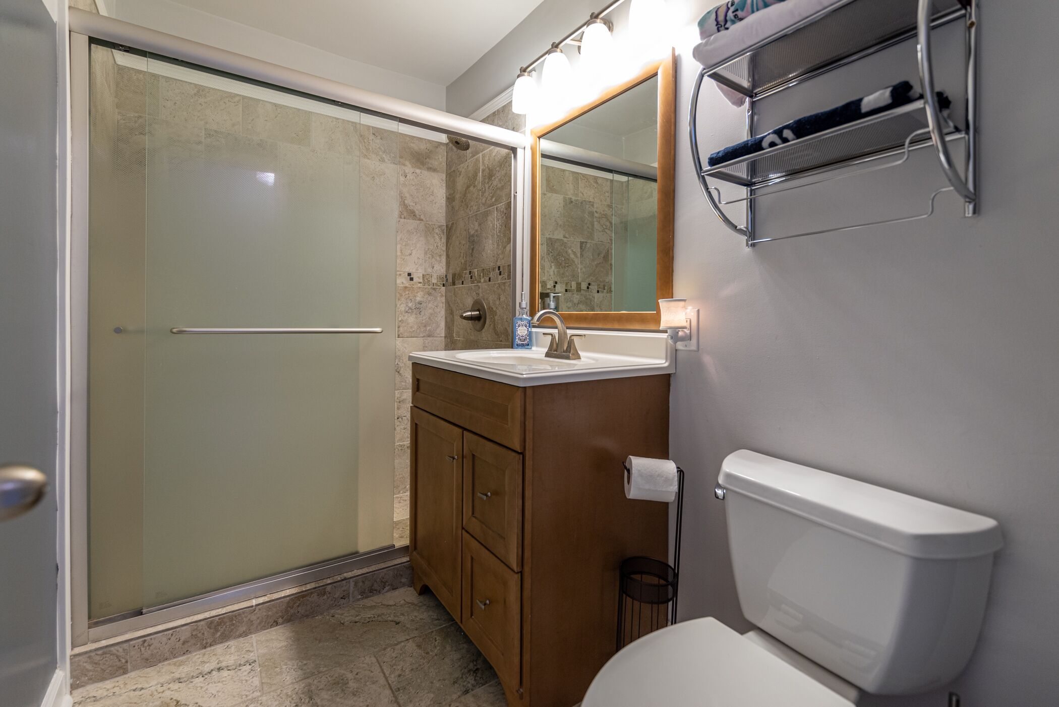 Een badkamer met een douchecabine van glas, een houten wastafelmeubel met een spiegel en een wit toilet.
