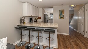 Une cuisine moderne avec des meubles blancs, un plan de travail en granit et un coin bar avec des tabourets.
