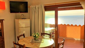 A dining area with a table, chairs, a television, a scale, and a view of the sea. - Apartment "of the violets "in the villa "Refuge of Seagulls" (Trinità d'Agultu e Vignola)