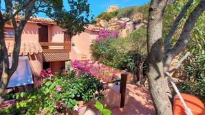 A traditional building with a tiled roof, a wooden balcony, and a garden with pink flowers. - Apartment "of the violets "in the villa "Refuge of Seagulls" (Trinità d'Agultu e Vignola)