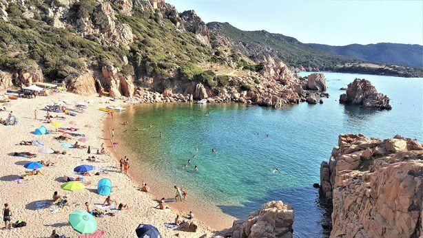 A beach with clear turquoise water, rocky cliffs, and umbrellas. - Apartment "of the violets "in the villa "Refuge of Seagulls" (Trinità d'Agultu e Vignola)