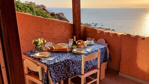 A table set for two with a view of the sea, a bottle of wine, and a fruit bowl. - Apartment "of the violets "in the villa "Refuge of Seagulls" (Trinità d'Agultu e Vignola)