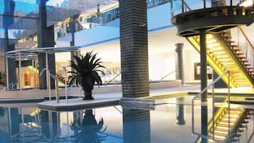 A modern indoor pool area with a central column, a staircase, and a reflection pool.