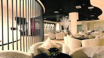 A modern lounge area with round tables, comfortable seating, and a unique ceiling design.
