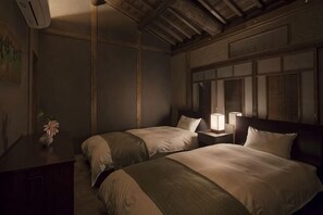 A room with two beds, a nightstand with a lamp, a dresser, and a painting on the wall.