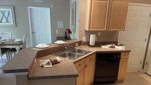 A kitchen with a built-in dishwasher, wooden cabinets, a countertop with a sink, and a dining area with chairs and a table. - Stunning Stay Disney Orlando, 2Bed / 2Bath Condo (Davenport)