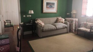 A living room with a green wall, a checkered sofa, a floral armchair, a small table with a lamp, and a framed picture on the wall. - Churrut Hotel (Vera de Bidasoa)