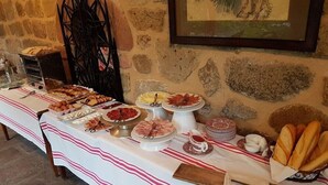 A buffet table with various food items and utensils, set against a stone wall with a framed picture. - Churrut Hotel (Vera de Bidasoa)