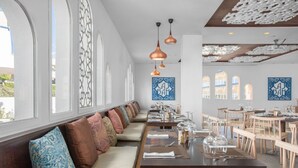 En restaurang med ett långt, gemensamt bord, bekväma sittplatser, hängande lampor och dekorativ väggkonst.