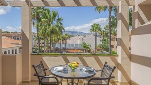 A balcony with a table set for two, overlooking a cityscape with palm trees and buildings. - Family 2-Bed Apartment | Costa del Sol | Sleeps 6 (Las Lagunas de Mijas)