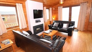 Un salon chaleureux avec une cheminée, un canapé en cuir noir, un téléviseur et un plancher en bois.