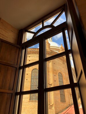 A room with a large window overlooking a historic building with arched windows and a dome. - Flore Apartment (Cuenca)