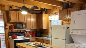 A kitchen with wooden cabinets, a microwave, a stove, a refrigerator, and a checkered cloth on the counter. - Private creek cabin with hot tub nestled in the foothills of Cheat mountain  (Huttonsville)