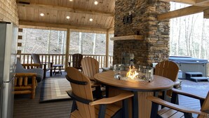 A wooden deck with a stone fireplace, outdoor seating, and a view of trees. - Private creek cabin with hot tub nestled in the foothills of Cheat mountain  (Huttonsville)