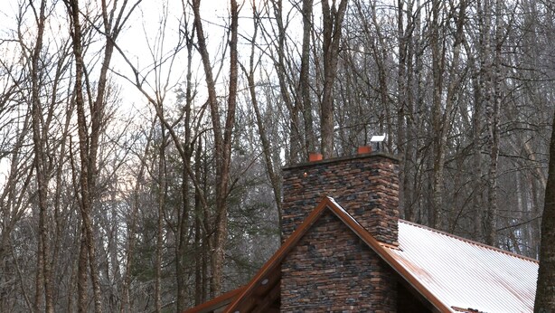 A lodge with a stone chimney, wooden deck, and a view of a flowing river. - Private creek cabin with hot tub nestled in the foothills of Cheat mountain  (Huttonsville)