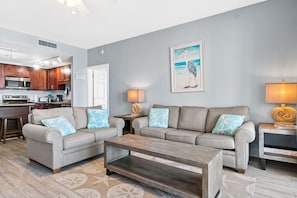 A modern living room with a grey sofa, two armchairs, a wooden coffee table, and a kitchen in the background. - Beach view with a large private balcony. (Panama City Beach)