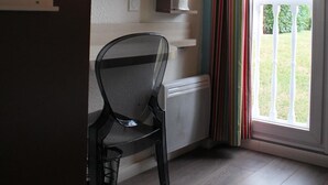 A room with a chair, a radiator, a shelf with items, and a view through a door with curtains.
