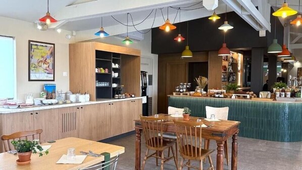 A restaurant with wooden furniture, a bar area, and colorful pendant lights.
