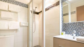 A bathroom with a toilet, a shower with a glass door, a sink with a mirror, and tiled walls.