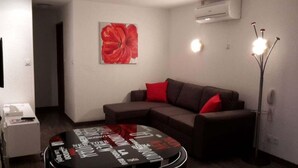 A living room with a sectional sofa, a round coffee table with magazine titles, a red flower painting, and a floor lamp.