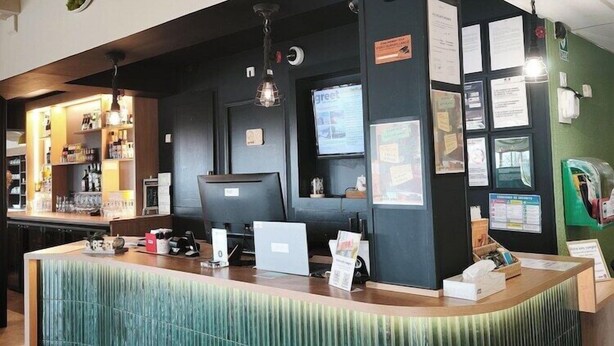 A reception desk with a 'greet' sign, a computer, and various informational posters.