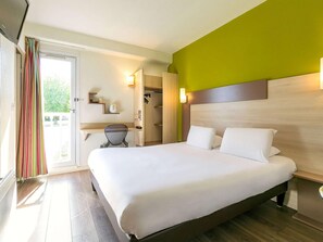 A hotel room with a large bed, a desk, a chair, a wardrobe, and a television.