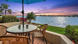 A patio with a round table and wicker chairs, overlooking a body of water with a cityscape in the background. - CLUB BAHIA WATERFRONT - COUNTRY CLUB USAGE (st . petersburg)