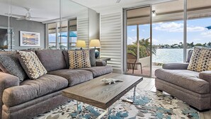 A modern living room with a grey sofa, a wooden coffee table, and a view of the water. - CLUB BAHIA WATERFRONT - COUNTRY CLUB USAGE (st . petersburg)