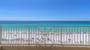 A beach view from a balcony with a railing, clear blue sky, and turquoise sea.