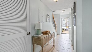 A hallway with a closed white door, a wooden console table with a lamp, and a staircase leading to another room. - Southbay by the Gul 69 Updated Poolside Unit 75 Yards from Beach (Destin)
