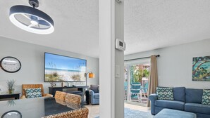 A modern living room with a large flat-screen TV, wicker furniture, and a view of the beach through the glass door. - Southbay by the Gul 69 Updated Poolside Unit 75 Yards from Beach (Destin)