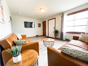 Un salon avec un canapé, des fauteuils, une table basse et un téléviseur fixé au mur.