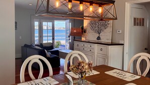 A dining area with a wooden table, white chairs, and a chandelier. - Enjoy Gorgeous Sunsets From Your Waterfront Beach House. (Hull)