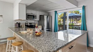 A modern kitchen with granite countertops, stainless steel appliances, and a breakfast bar with stools. - 50 steps to uncrowded beach - 2 king beds - Pac Man arcade - summer beach fun! (Englewood)